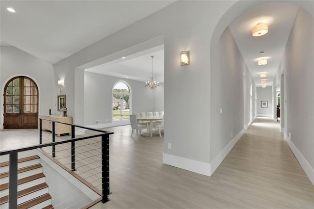 corridor with a notable chandelier, french doors, and light hardwood / wood-style flooring