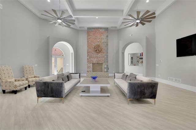 living room featuring beam ceiling, light wood-type flooring, a fireplace, and a high ceiling