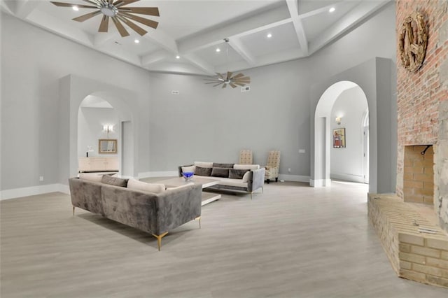 living room featuring beam ceiling, a towering ceiling, light hardwood / wood-style floors, and a brick fireplace