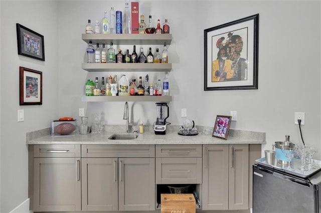 bar with gray cabinetry, light stone countertops, sink, and stainless steel refrigerator