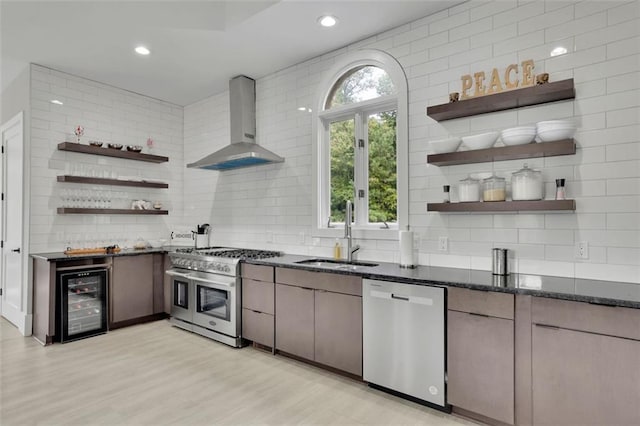 kitchen featuring sink, wall chimney exhaust hood, wine cooler, appliances with stainless steel finishes, and light wood-type flooring