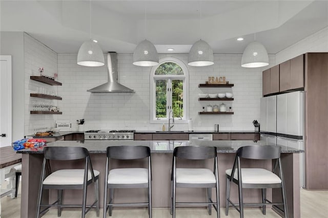 kitchen with sink, wall chimney range hood, backsplash, decorative light fixtures, and a breakfast bar