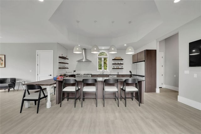 kitchen featuring a kitchen bar, wall chimney exhaust hood, dark brown cabinetry, pendant lighting, and light hardwood / wood-style floors