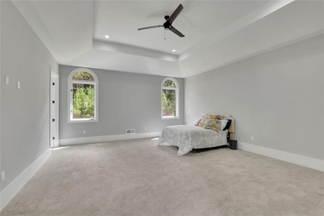 carpeted bedroom featuring a tray ceiling, multiple windows, and ceiling fan