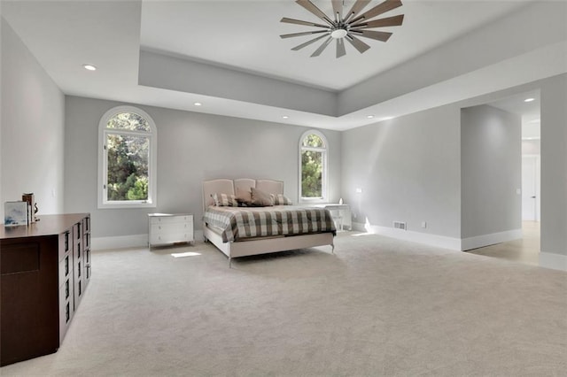 carpeted bedroom with ceiling fan and a raised ceiling