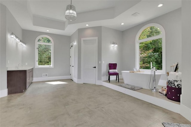 bathroom featuring a notable chandelier, a washtub, a raised ceiling, and vanity