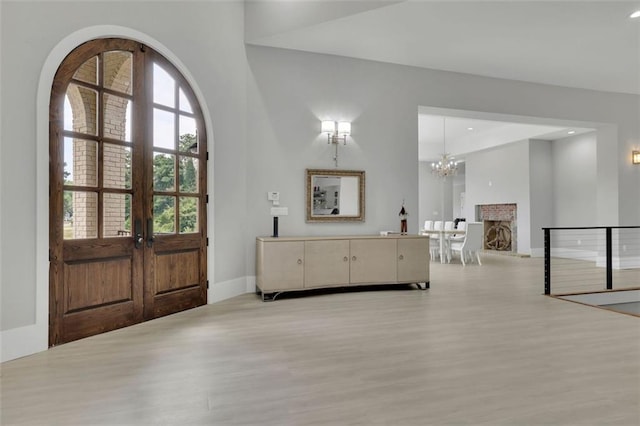 entrance foyer with a fireplace, french doors, light hardwood / wood-style floors, and a notable chandelier