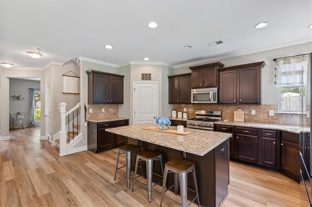 4275 Hunters Walk Way, Cumming, GA 30028 - kitchen featuring appliances with stainless steel finishes, a kitchen breakfast bar, dark brown cabinetry, light wood-style flooring, and recessed lighting