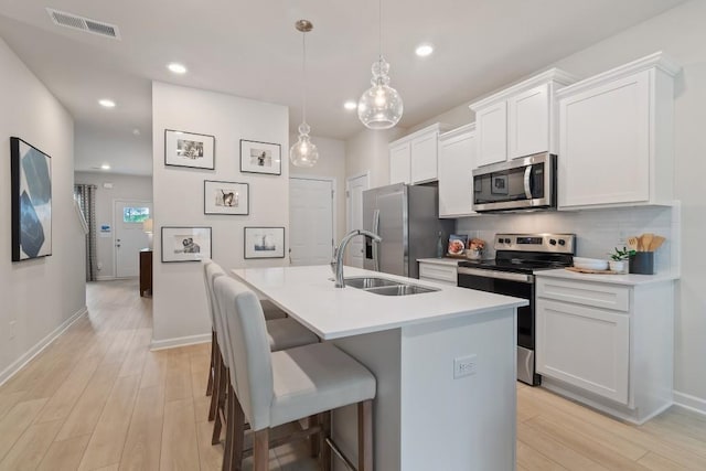 kitchen with appliances with stainless steel finishes, a sink, an island with sink, light wood-style flooring, and recessed lighting
