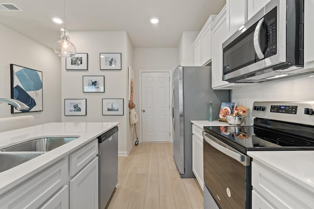 kitchen featuring appliances with stainless steel finishes, a sink, white cabinetry, light wood finished floors, and light countertops