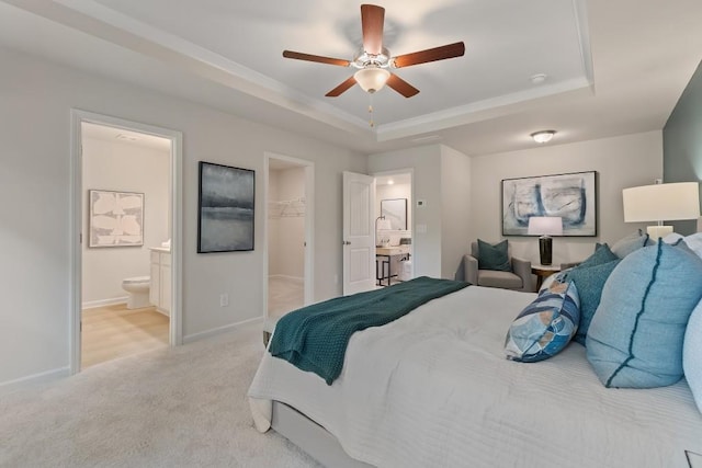 bedroom with a raised ceiling, light colored carpet, baseboards, and a walk in closet