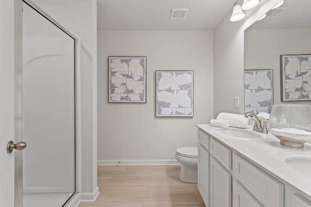 bathroom featuring a stall shower, baseboards, wood finished floors, double vanity, and toilet