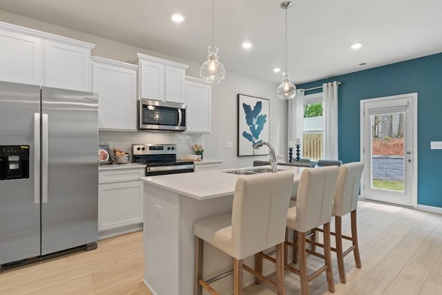 kitchen with appliances with stainless steel finishes, light wood-style flooring, decorative backsplash, an island with sink, and white cabinets