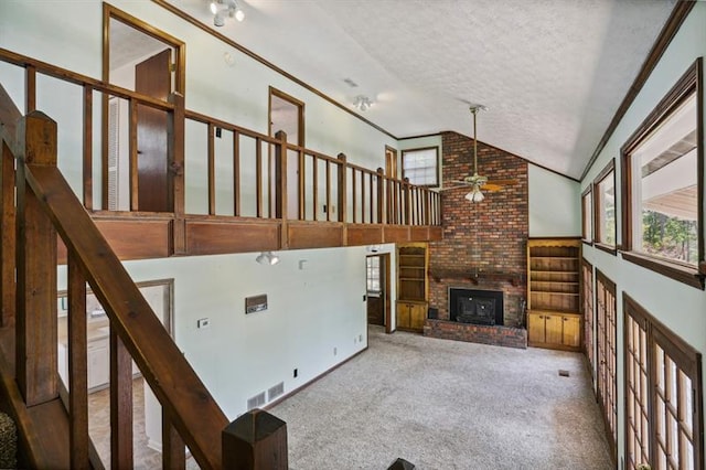 unfurnished living room with ceiling fan, a brick fireplace, vaulted ceiling, carpet floors, and a textured ceiling