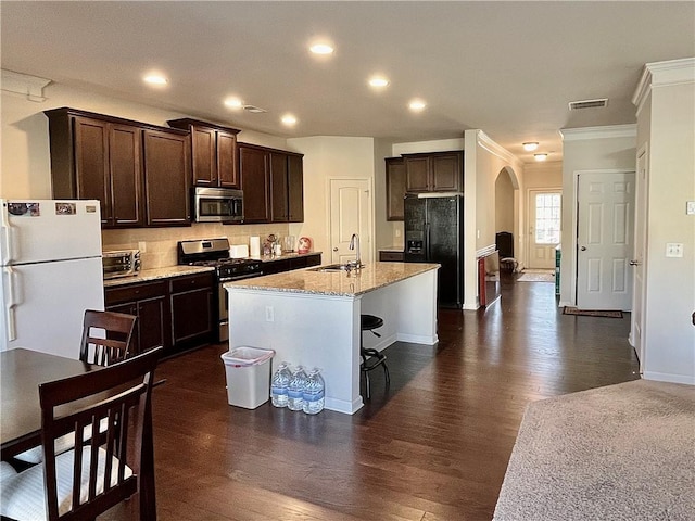 kitchen featuring arched walkways, stainless steel appliances, visible vents, a sink, and dark brown cabinetry