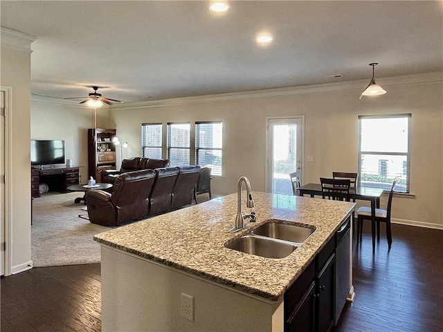 kitchen with decorative light fixtures, crown molding, a kitchen island with sink, a sink, and dishwashing machine