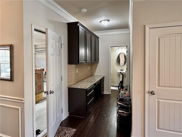 kitchen with light stone counters, crown molding, decorative backsplash, dark wood-type flooring, and dark cabinets