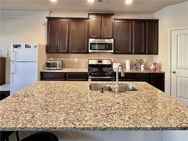 kitchen with decorative backsplash, appliances with stainless steel finishes, a sink, dark brown cabinets, and light stone countertops