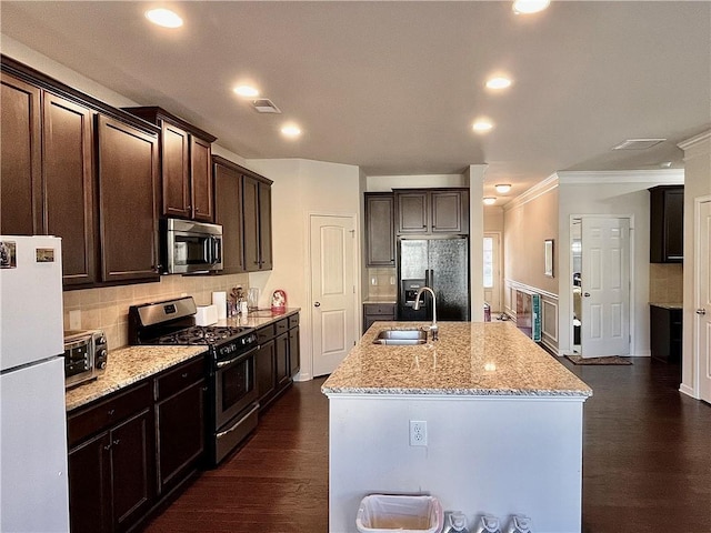 kitchen featuring dark wood-style floors, appliances with stainless steel finishes, light stone counters, a kitchen island with sink, and a sink