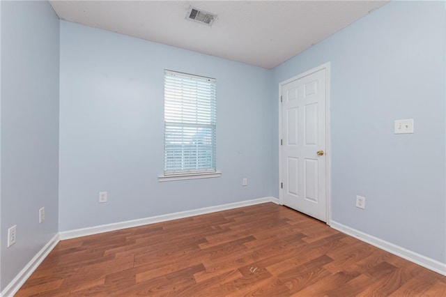 empty room with wood finished floors, visible vents, and baseboards