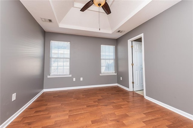 empty room with a tray ceiling, visible vents, baseboards, and wood finished floors