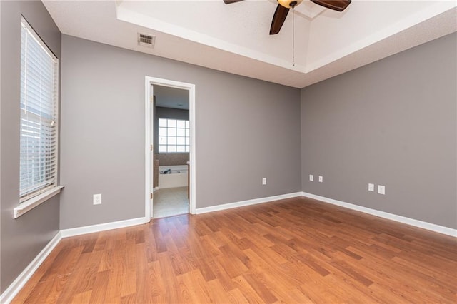 unfurnished room with wood finished floors, visible vents, baseboards, ceiling fan, and a raised ceiling