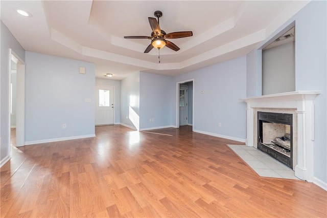 unfurnished living room with baseboards, a raised ceiling, a tiled fireplace, and light wood finished floors