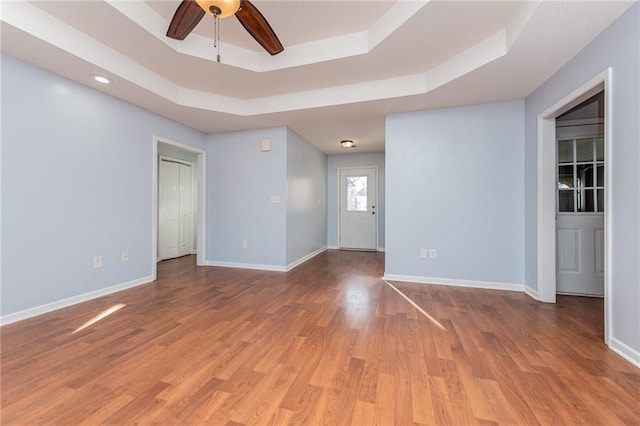 unfurnished room with ceiling fan, baseboards, a raised ceiling, and light wood-style flooring