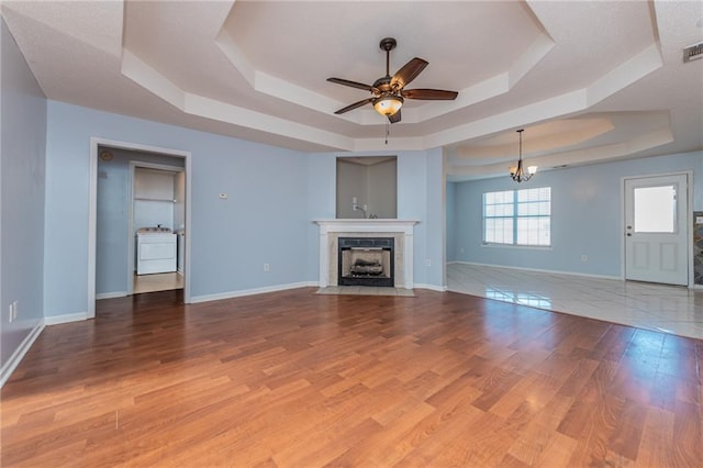 unfurnished living room featuring a tray ceiling, a fireplace with flush hearth, baseboards, and wood finished floors