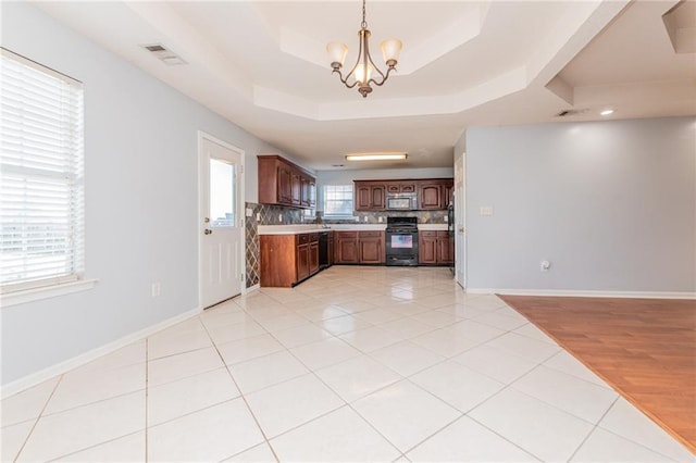 kitchen featuring a raised ceiling, black appliances, light tile patterned flooring, light countertops, and baseboards