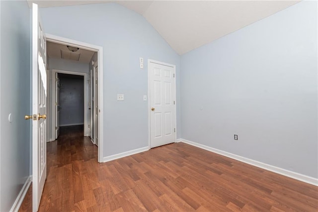 unfurnished bedroom featuring vaulted ceiling, attic access, wood finished floors, and baseboards