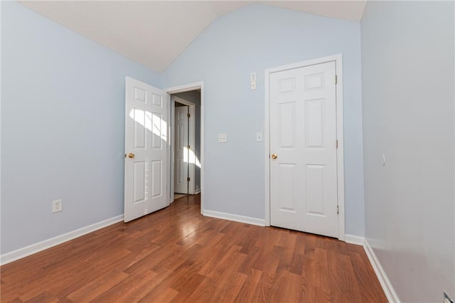 unfurnished bedroom featuring vaulted ceiling, baseboards, and wood finished floors