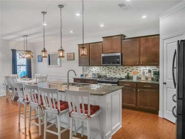 kitchen featuring a kitchen bar, sink, hanging light fixtures, an island with sink, and stainless steel appliances