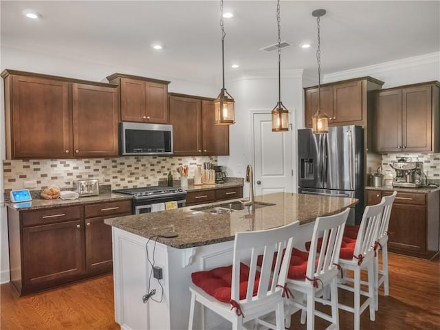 kitchen featuring sink, decorative light fixtures, a center island with sink, dark stone counters, and stainless steel appliances