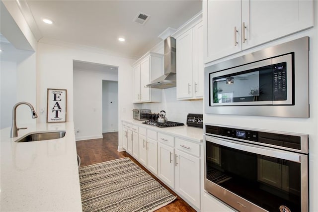 kitchen featuring appliances with stainless steel finishes, wall chimney exhaust hood, sink, dark wood-type flooring, and white cabinetry