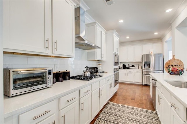 kitchen with light hardwood / wood-style floors, light stone countertops, appliances with stainless steel finishes, white cabinets, and wall chimney exhaust hood