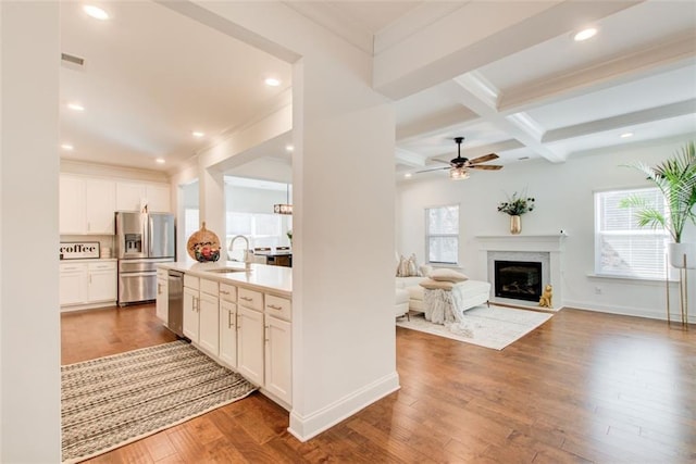 kitchen with beamed ceiling, coffered ceiling, white cabinets, sink, and stainless steel appliances