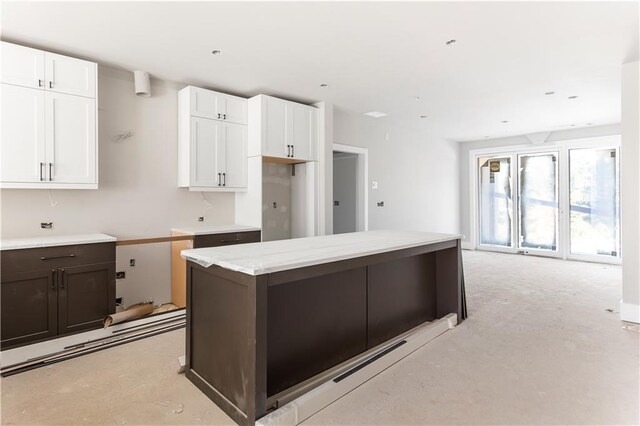 kitchen featuring white cabinetry, dark brown cabinetry, light stone countertops, and a kitchen island