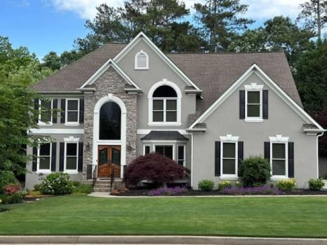 view of front facade with a front yard, french doors, stone siding, and stucco siding