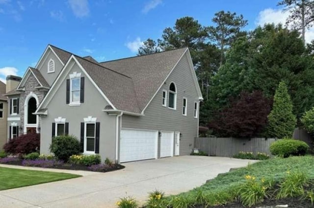 traditional-style home featuring an attached garage, driveway, and fence