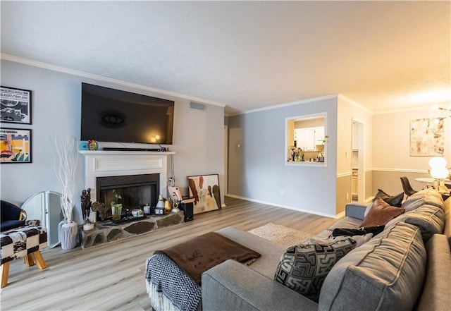 living area with visible vents, a fireplace with raised hearth, ornamental molding, and wood finished floors