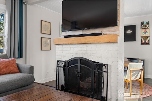 interior space featuring a brick fireplace, baseboards, crown molding, and wood finished floors