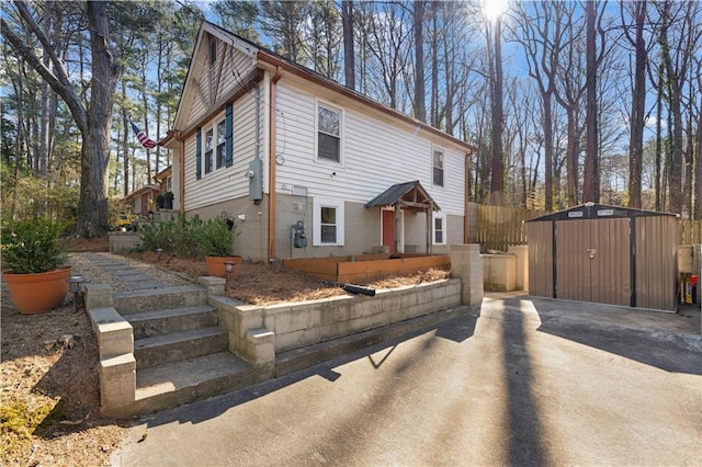 view of front of property featuring a storage shed, fence, concrete driveway, and an outdoor structure