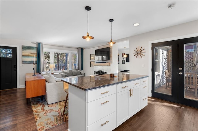 kitchen with dark wood-type flooring, french doors, a fireplace, and dark stone countertops