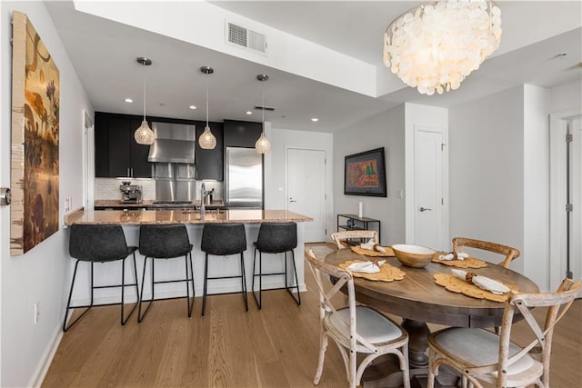 kitchen featuring built in fridge, dark hardwood / wood-style floors, hanging light fixtures, kitchen peninsula, and wall chimney range hood