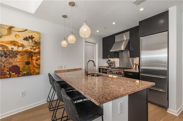 kitchen with wall chimney range hood, sink, a breakfast bar area, appliances with stainless steel finishes, and kitchen peninsula