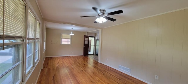 spare room featuring a ceiling fan, visible vents, baseboards, light wood finished floors, and ornamental molding