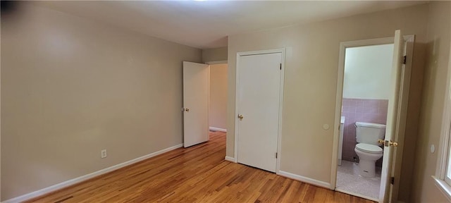 unfurnished bedroom with baseboards, light wood-style flooring, and ensuite bath