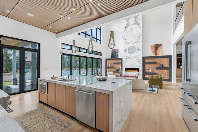 kitchen with light wood-style flooring, modern cabinets, appliances with stainless steel finishes, a sink, and a premium fireplace