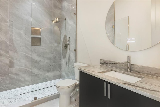 bathroom with toilet, tiled shower, and vanity